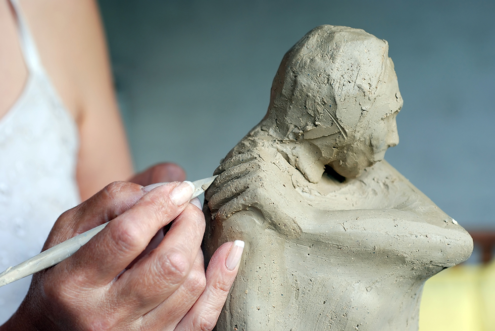 A close up of a hand carving out a sculpture of a human